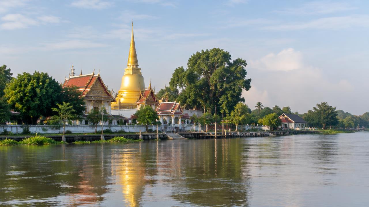 วัดริมแม่น้ำเจ้าพระยาในอ่างทอง มีเจดีย์สีทองและต้นไม้เขียวโดยรอบ