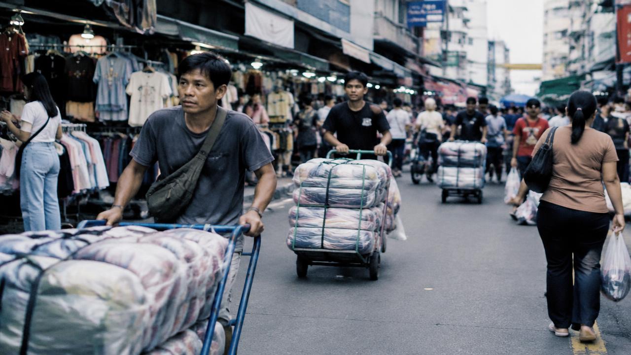 คนงานเข็นรถเข็นที่มีห่อเสื้อผ้ากองสูงในตลาดค้าส่ง