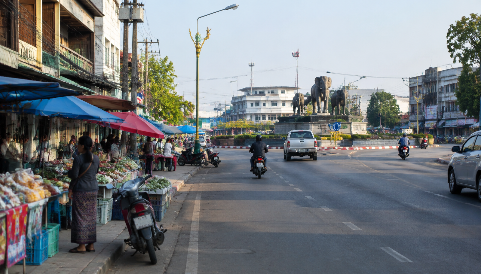 ถนนในเมืองสุรินทร์ยามเช้า มีตลาดริมทางและอนุสาวรีย์ช้างที่วงเวียน
