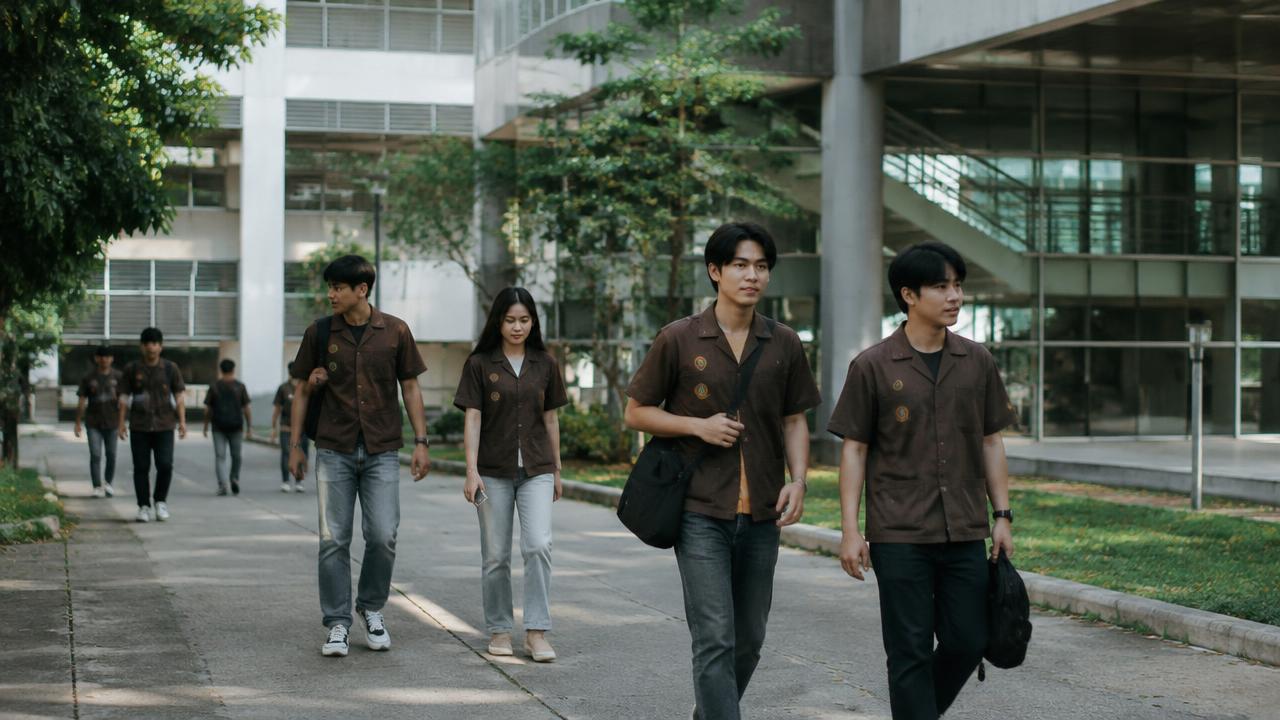 นักศึกษาในชุดเสื้อช็อปเดินผ่านอาคารในมหาวิทยาลัย ยามบ่าย