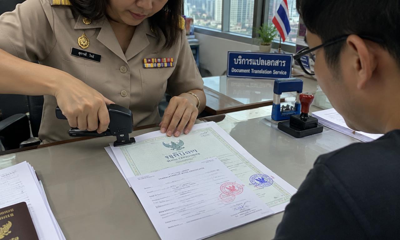 泰国工作人员将翻译件与带官方印章的出生证明原件装订在一起,中国客户在旁观看